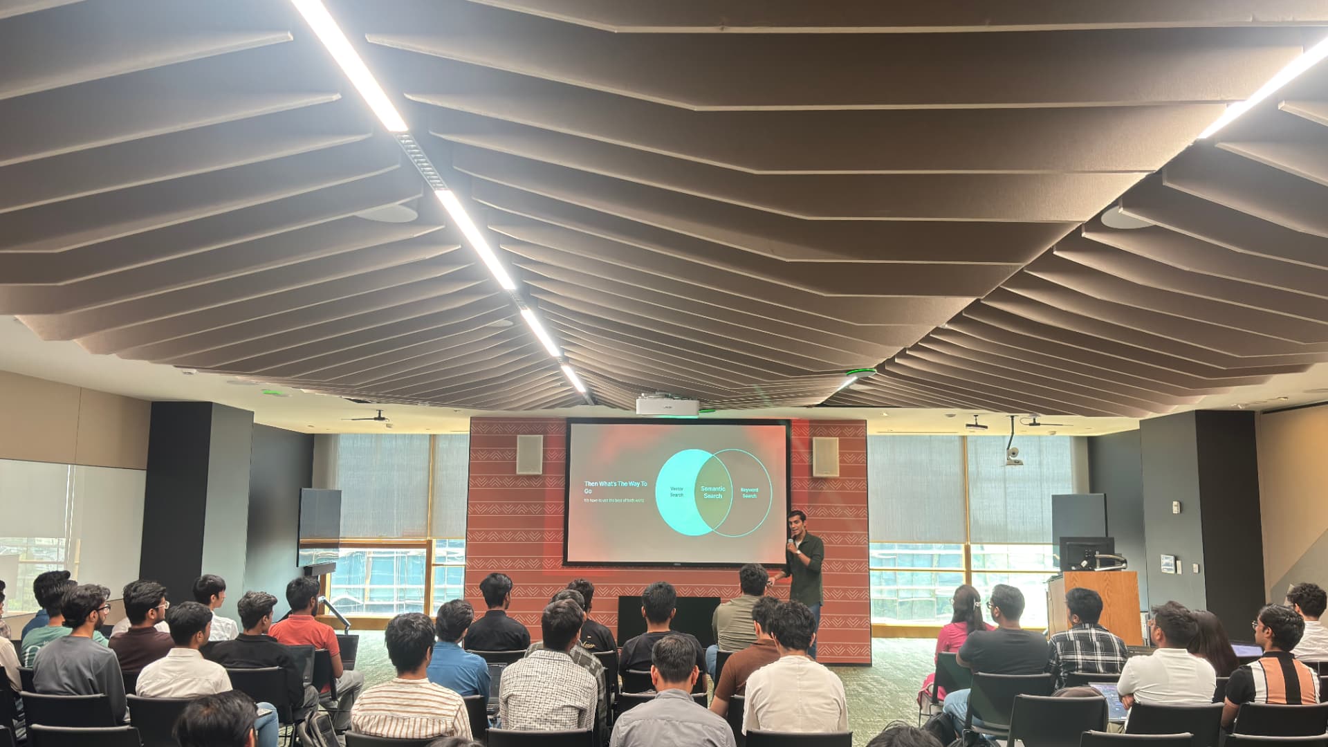 Speaker presenting to a seated audience in an auditorium during a technical session